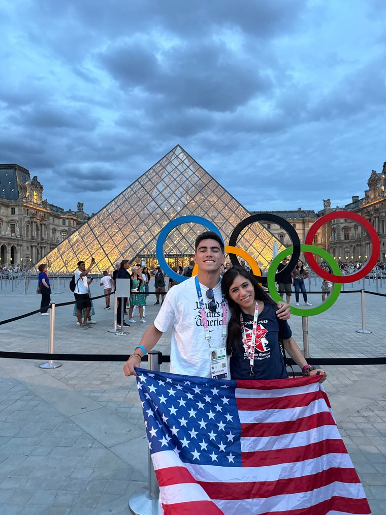Veronica and Mitchell holding a US flag in front of the Olympic rings at the Louvre in Paris